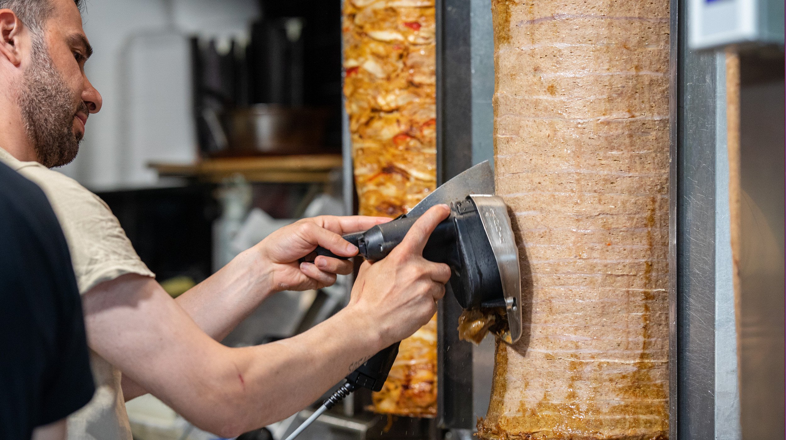 Döner-Bude Mitarbeiter schneidet Fleisch ab.