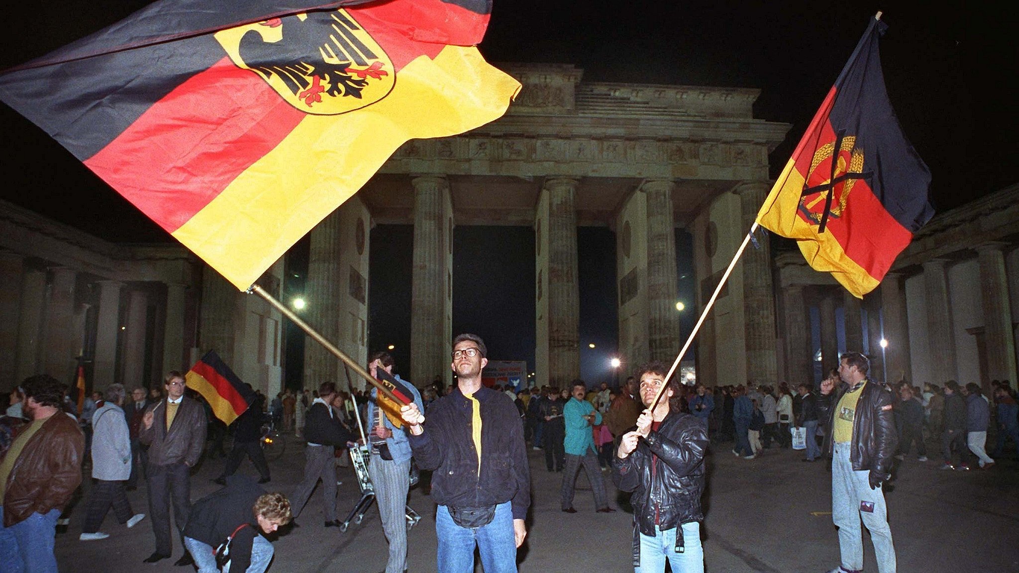 Jugendliche schwenken in der Nacht zum 3. Oktober 1990 vor dem Brandenburger Tor in Berlin die Deutsche Fahne (l) und die Fahne der DDR, auf der das DDR-Emblem durchgestrichen ist.