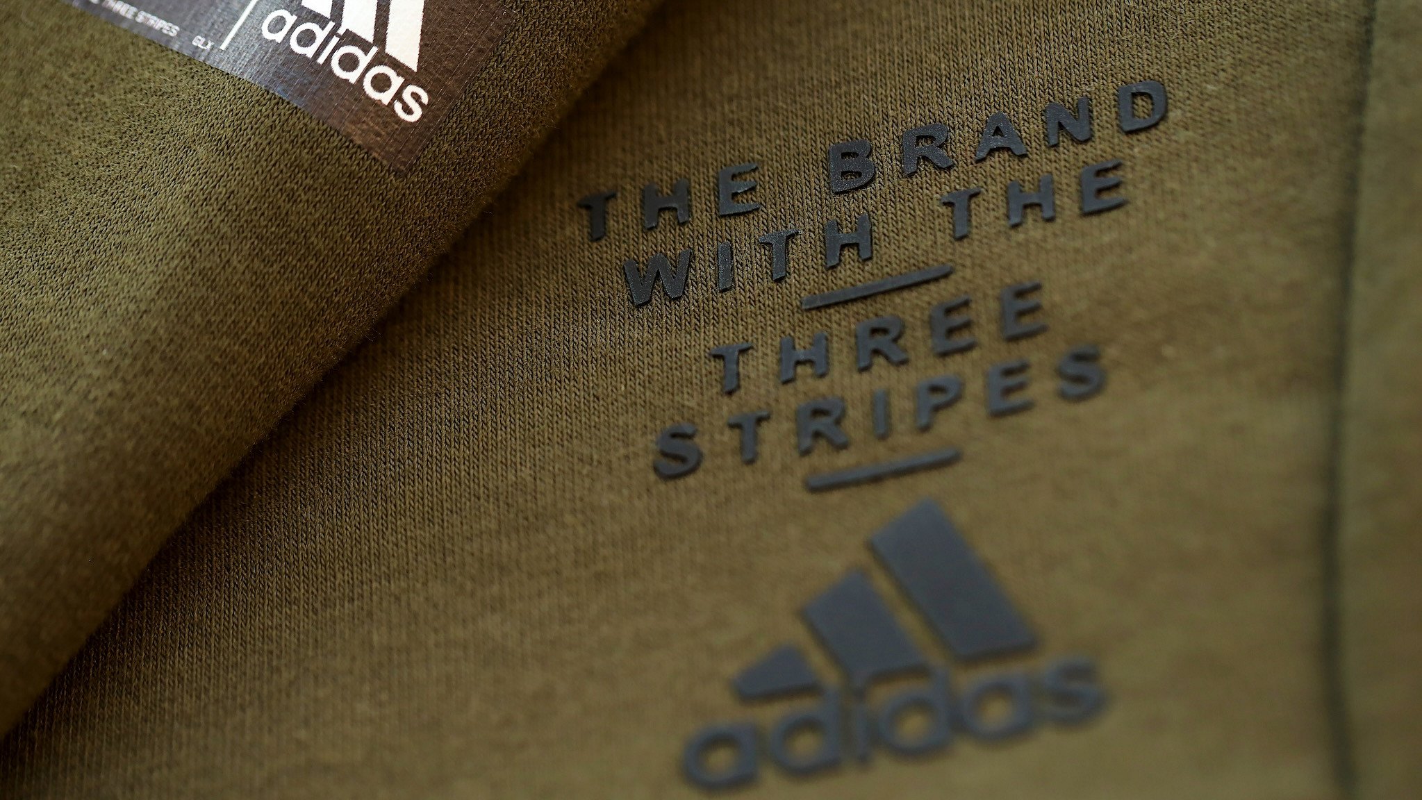 Olivgrüner Modeartikel von Adidas mit Aufdruck "Adidas - The brand with three stripes"