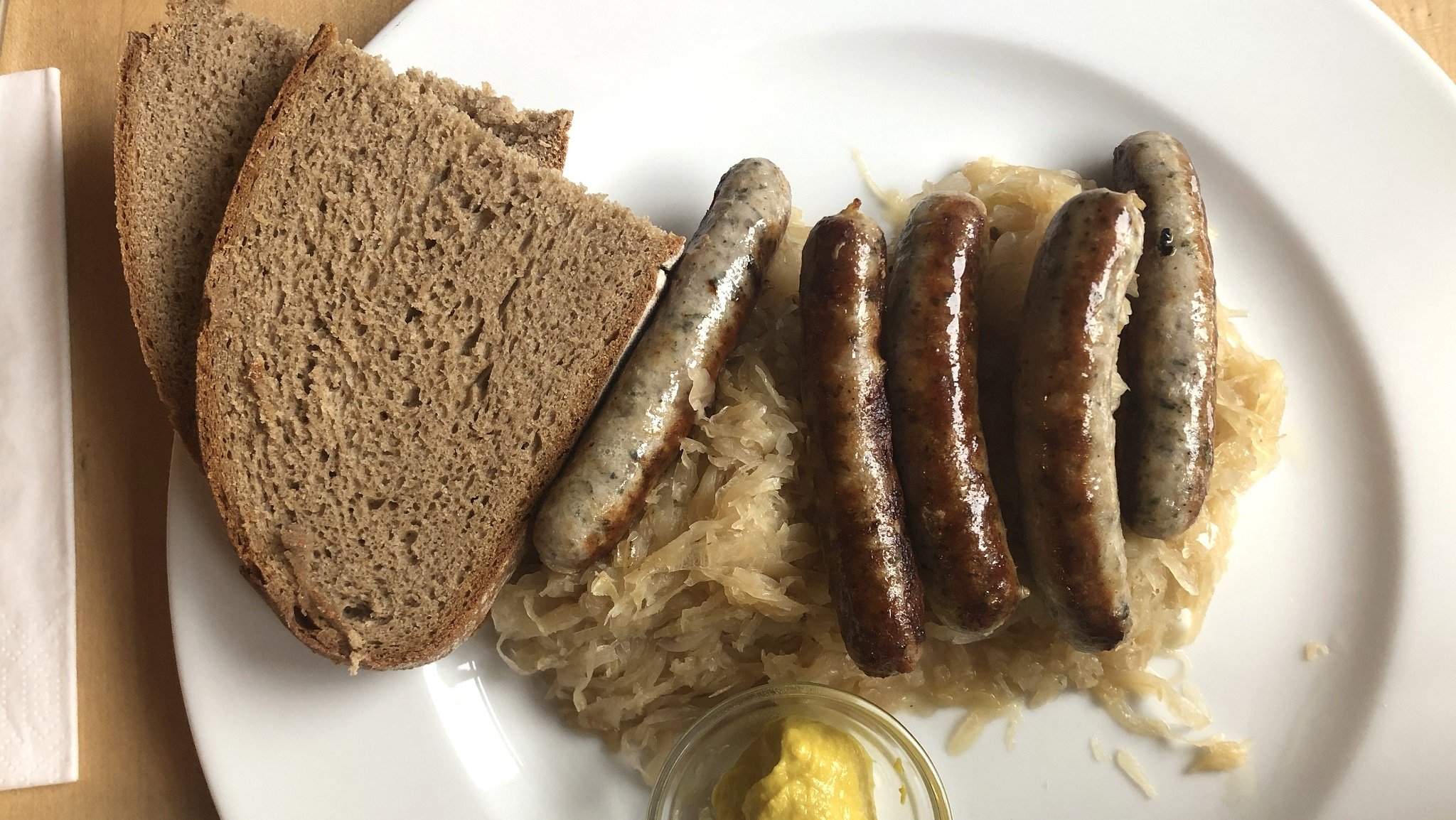 Nürnberger Rostbratwürste, Sauerkraut und zwei Scheiben Brot liegen auf einem Teller